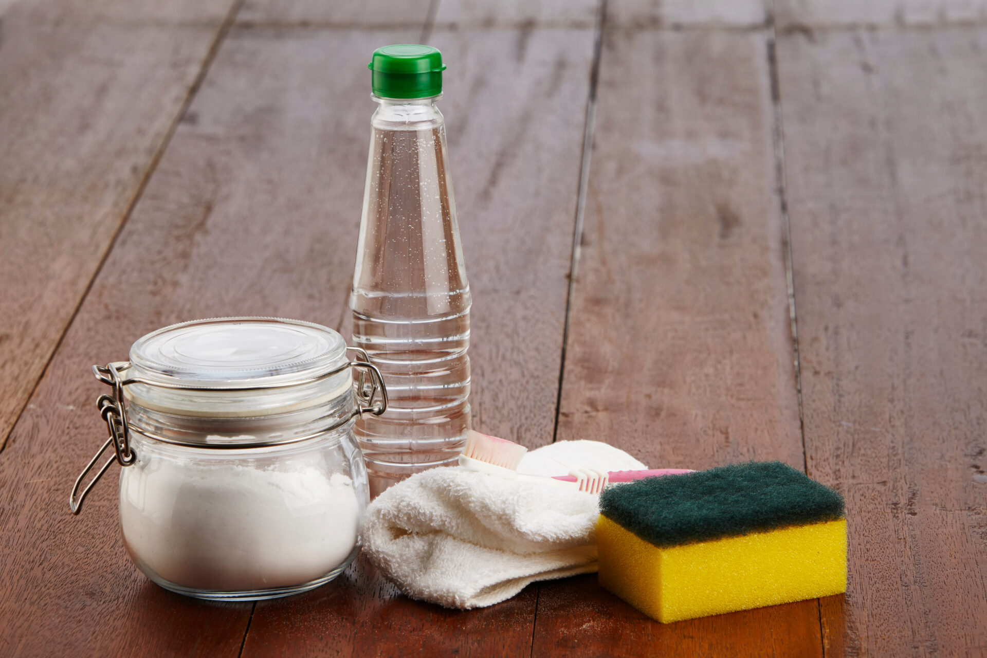 Household assortment of environmentally friendly cleaning supplies including baking soda, vinegar, a toothbrush, sponge, and a rag.